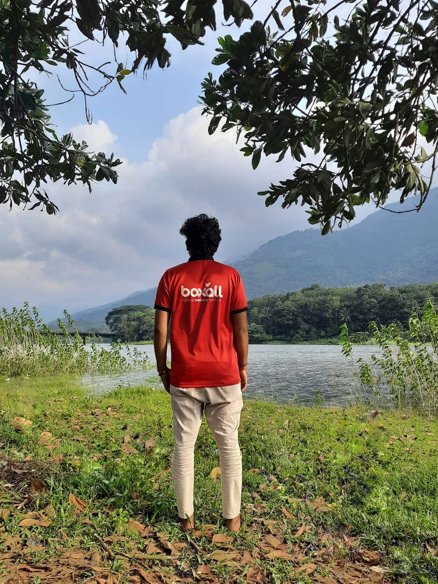 Someone in a red Boxall shirt seen from behind, looking out across a reservoir with wooded hills beyond