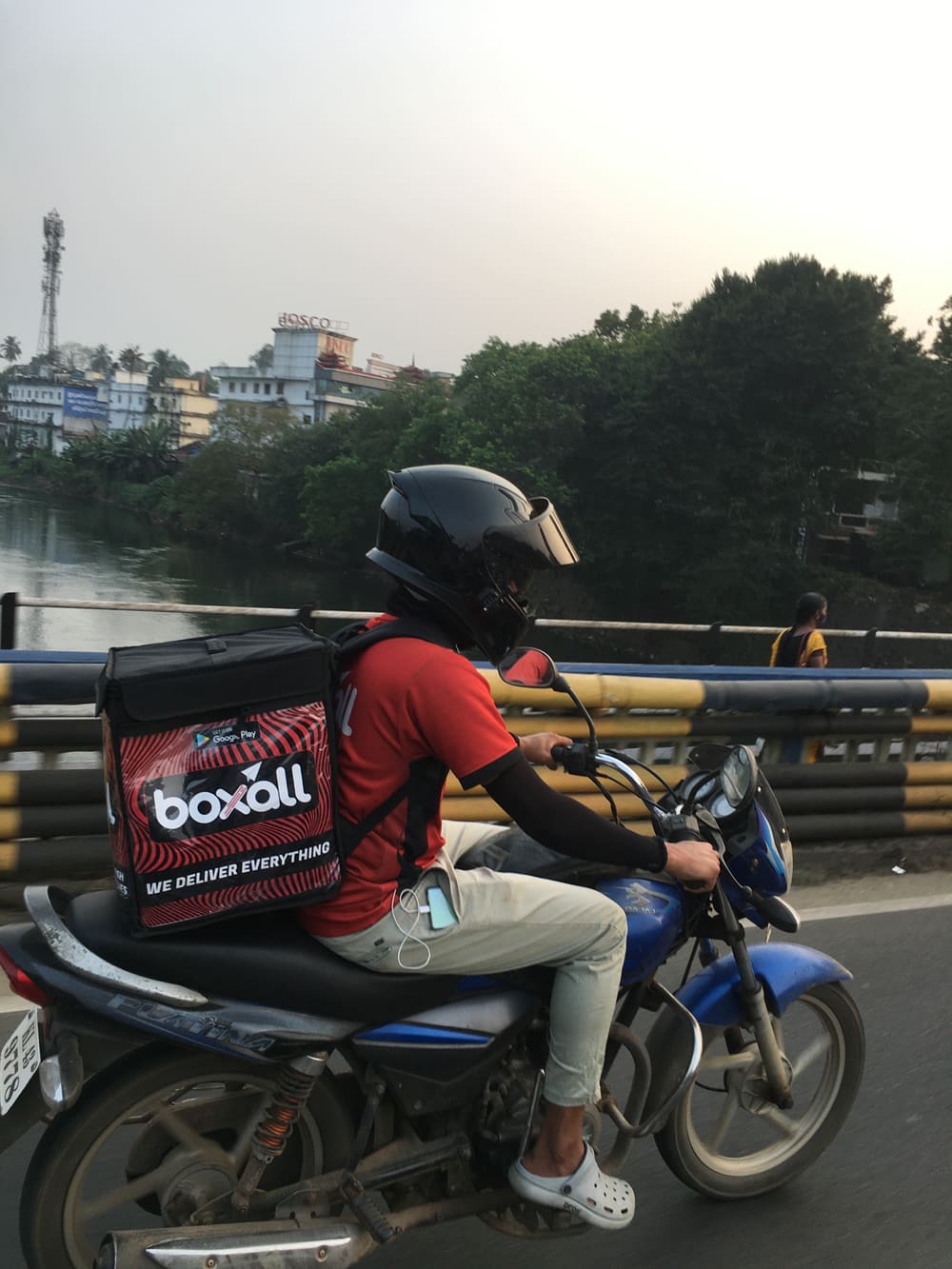 A Boxall rider crossing a bridge over a river at dawn, the delivery bag on the back reading boxall, we deliver everything