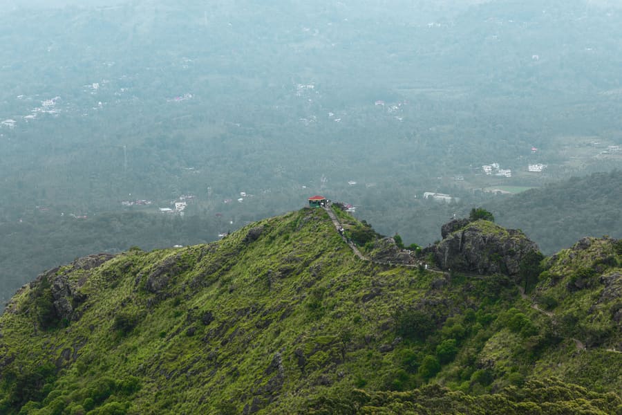 The hilltop ridge at Ilaveezhapoonchira seen from above, with a shelter on the summit and green slopes falling away on both sides