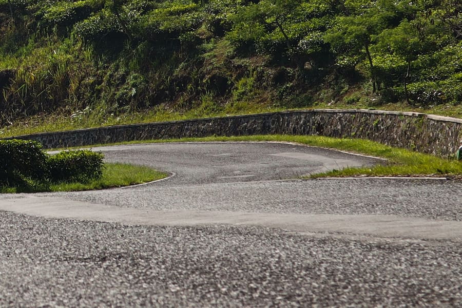 A road curving past planted slopes near Ilaveezhapoonchira, with layers of misty blue hills behind