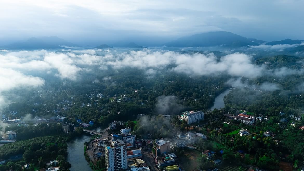 Thodupuzha seen from the air at dawn, the river winding past the town with low cloud lying over the ranges behind it