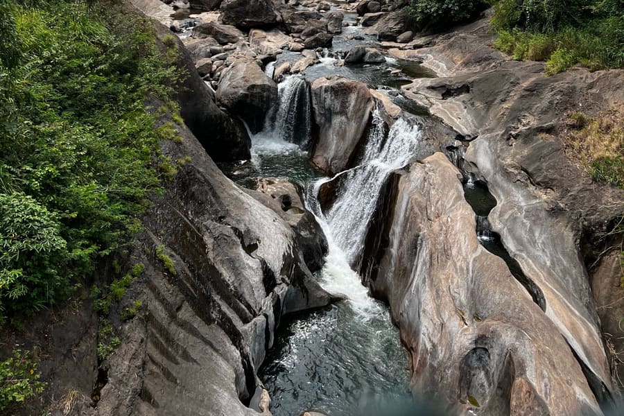 Water at Thommankuthu dropping between rock ledges into pools below, with forest on both banks