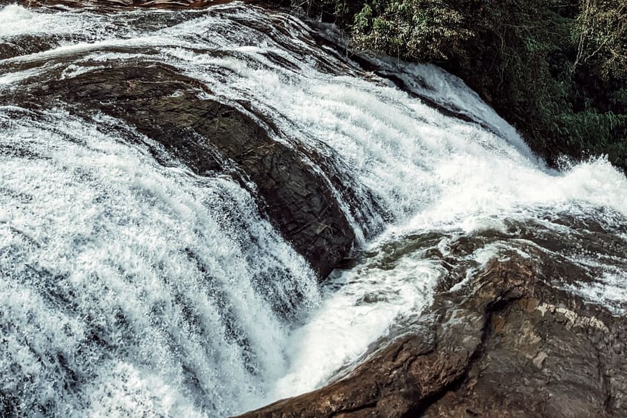 Water pouring over a broad rock ledge at Thommankuthu waterfalls